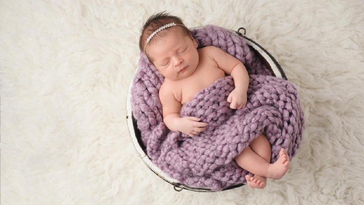 Sleeping, ten day old newborn baby girl swaddled in a light pink wrap. Shot in the studio on a white sheepskin rug.