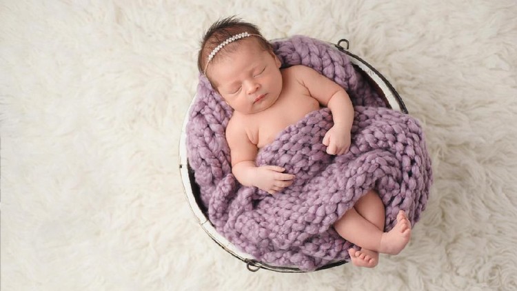 917059776 Sleeping, ten day old newborn baby girl swaddled in a light pink wrap. Shot in the studio on a white sheepskin rug.