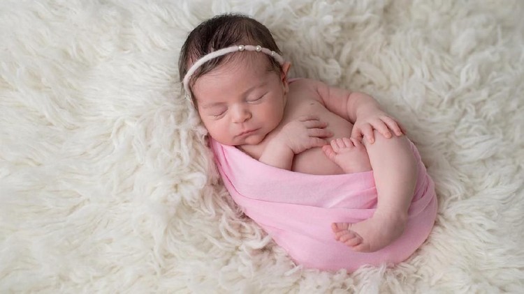 Sleeping, ten day old newborn baby girl swaddled in a light pink wrap. Shot in the studio on a white sheepskin rug.