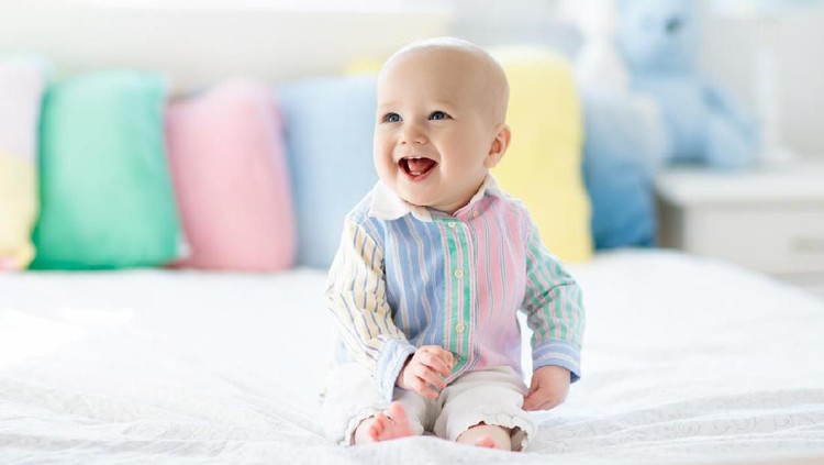 1136272104 Baby boy in white bedroom. Newborn child in bed with pastel color cushions. Nursery for children. Textile, pillows and bedding for kids. Family morning at home. New born kid tummy time with toy bear.
