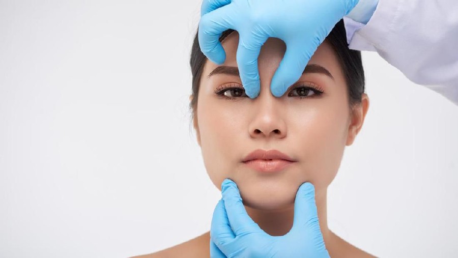 Hands of surgeon checking face construction of young Asian woman