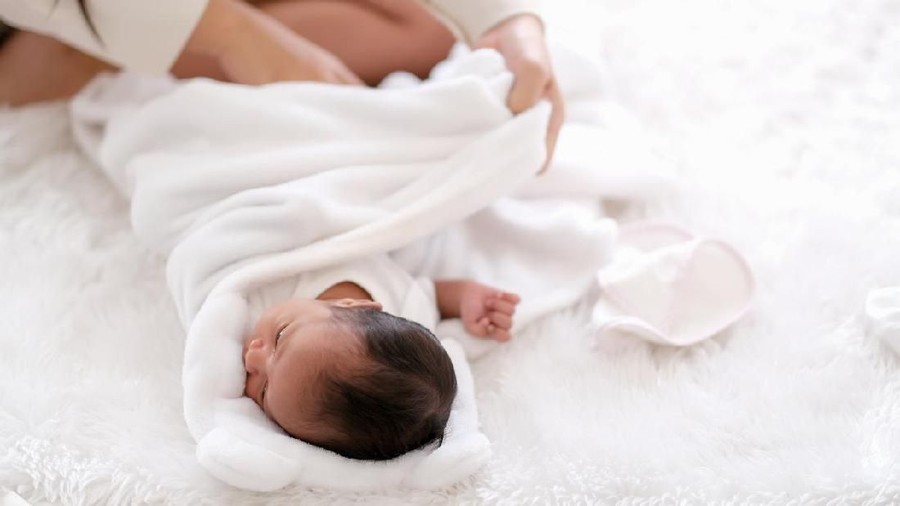 bedong Newborn baby was swaddling with white cloth by her mother and the activity is on bed.