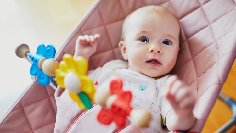 Baby Adorable baby girl sitting in bouncer and playing with colorful toys