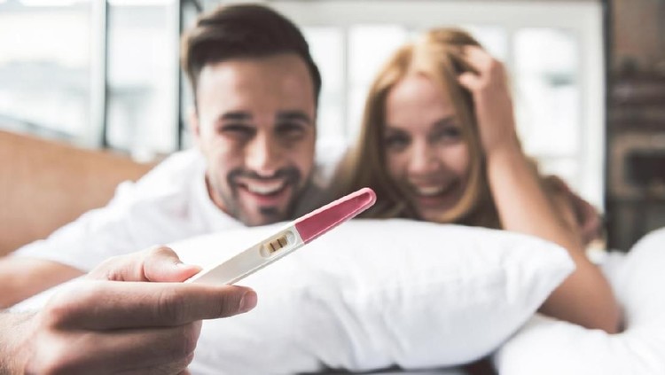 We are pregnant. Excited young man and woman are hugging and smiling. Focus on two strips on pregnancy test stick in male hand