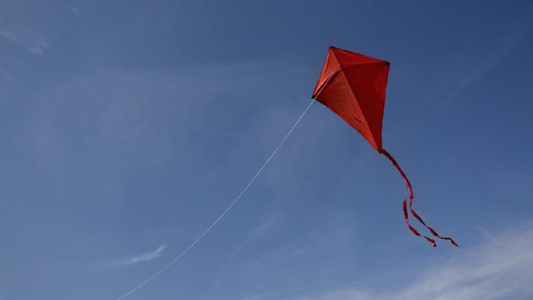 Ilustrasi layangan A red kite with a string flying against a blue sky.