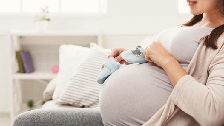 Kehamilan Pregnant woman holding tiny shoes near belly. Smiling expectant woman preparing for baby birth, joying maternity, copy space