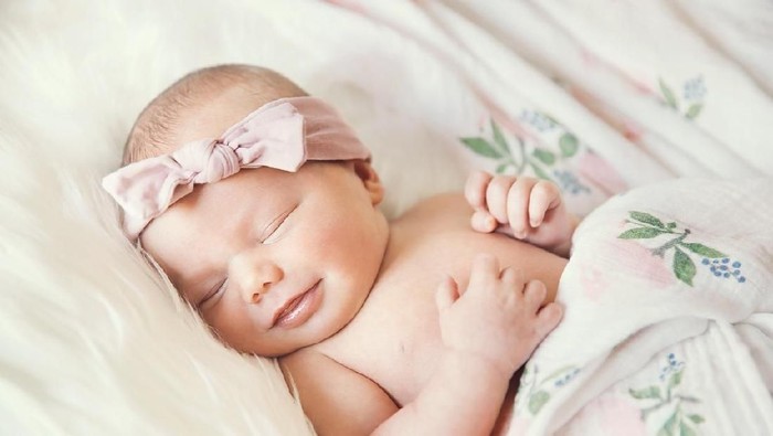 Charming beautiful lovely small female baby with plump cheeks creeps on bed, looks innocently on something, being naughty. Cute baby infant plays alone. Newborn kid crawls. Enthusiastic child