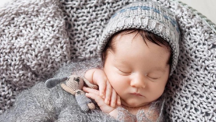 Sweet newborn baby sleeps in a basket. Beautiful newborn boy with bear toy.
