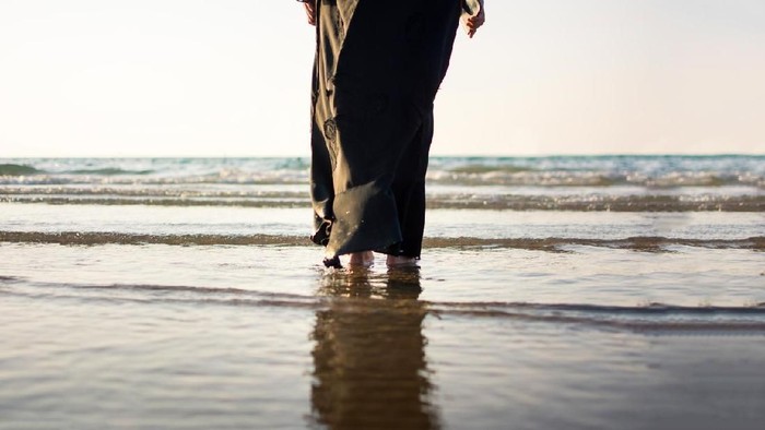 Woman in hijab standing on the beach back view