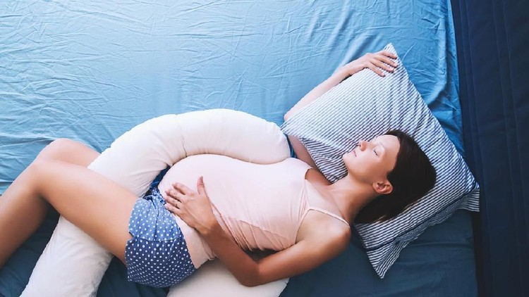 Beautiful pregnant woman relaxing or sleeping with tummy supporting pillow at bed. Young mother waiting of a baby. Concept of pregnancy, maternity, health care, gynecology, medicine.