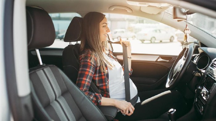 Pregnant happy woman driving with safety belt on in the car.