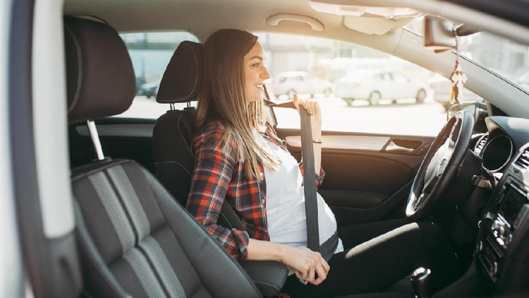 Pregnant happy woman driving with safety belt on in the car.