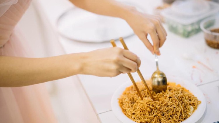 Woman preparing instant noodle on plate in kitchen