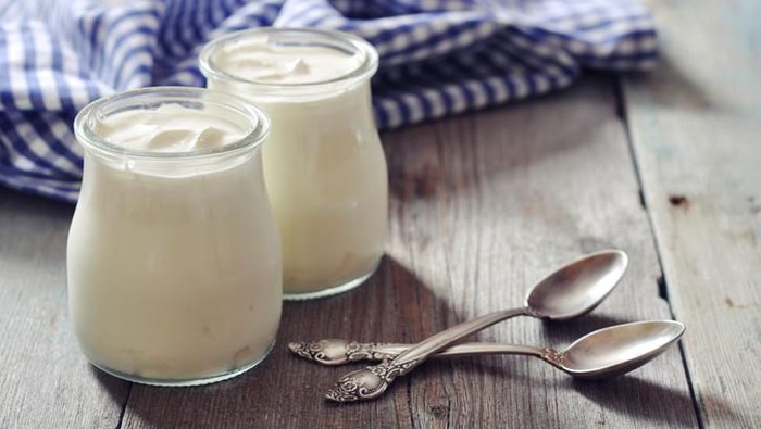 Greek yogurt in a glass jars with spoons on wooden background