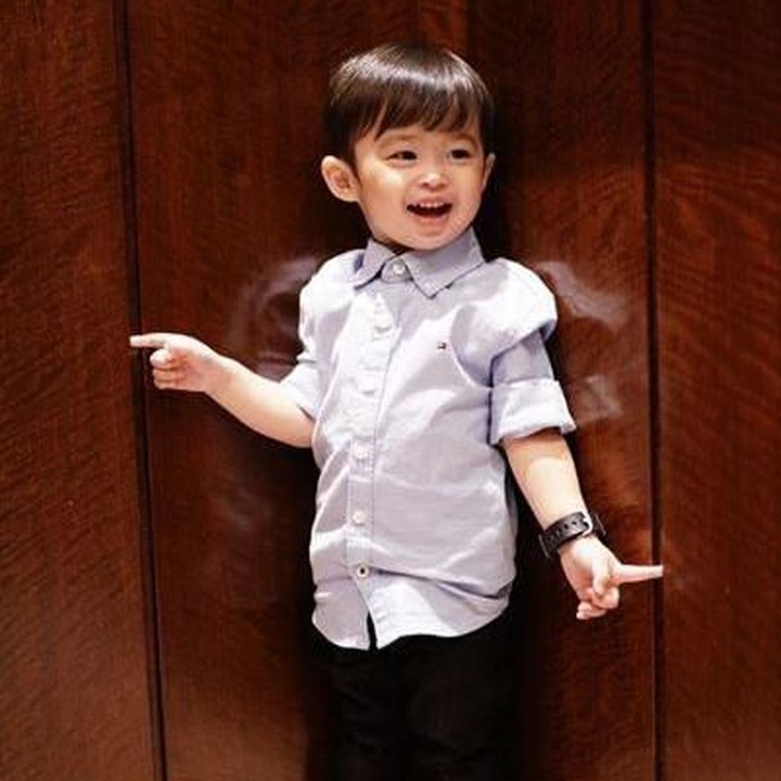 <p>Memakaikan anak kemeja panjang yang digulung ditambah celana bahan hitam bisa jadi inspirasi Bunda nih. Baju seperti yang dipakai Raphael ini bisa untuk acara-acara formal. (Foto: Instagram @sandradewi88)</p>