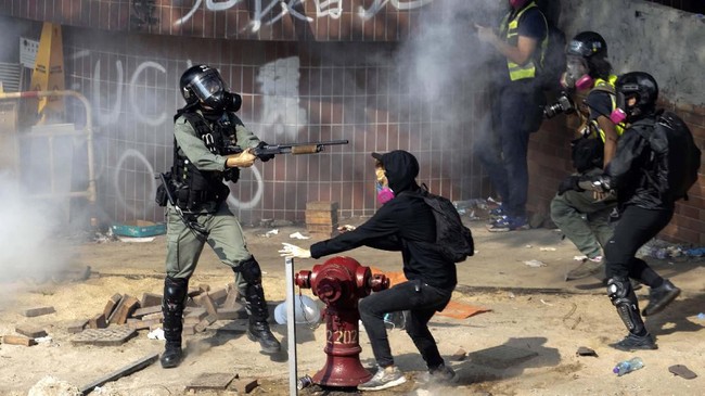 A policeman in riot gear points his weapon as protesters try to flee from the Hong Kong Polytechnic University in Hong Kong, Monday, Nov. 18, 2019. Hong Kong police have swooped in with tear gas and batons as protesters who have taken over the university campus make an apparent last-ditch effort to escape arrest. (AP Photo/Ng Han Guan)