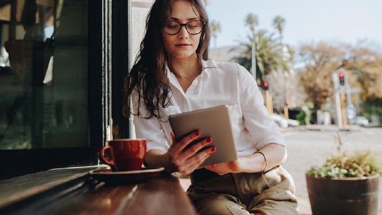 zodiak Woman sitting at a cafe working on digital tablet. Businesswoman sitting at cafe counter with a coffee using tablet computer.