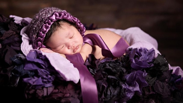 NB Beautiful sleeping multi ethnic baby girl wearing a knit purple bonnet.