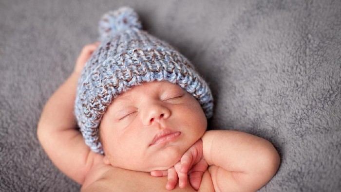 Close up, color image of a mixed race newborn baby boy sleeping peacefully and wearing knit cap, on gray textured background.