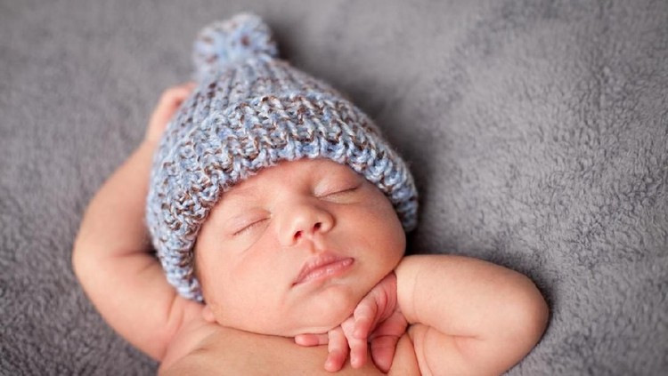 Close up, color image of a mixed race newborn baby boy sleeping peacefully and wearing knit cap, on gray textured background.