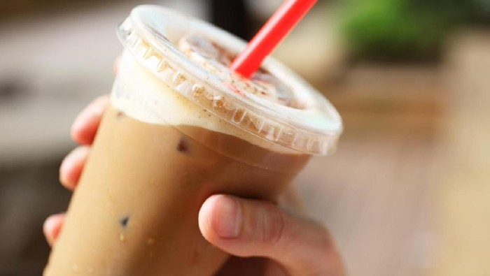 A cup of iced coffee in hand outdoors.