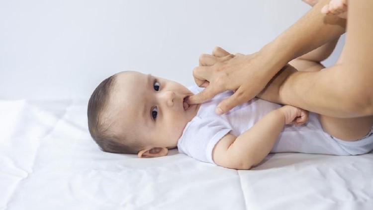 Baby boy teething pain. Little 6-month baby having teeth pains. Mother rubbing gel to her little baby boy's teeth. Medicine and health concept.
