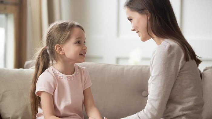 Loving family happy mother and cute child girl holding hands talking sitting on sofa at home, caring elder sister mom baby sitter having friendly trust conversation with preschool little kid daughter