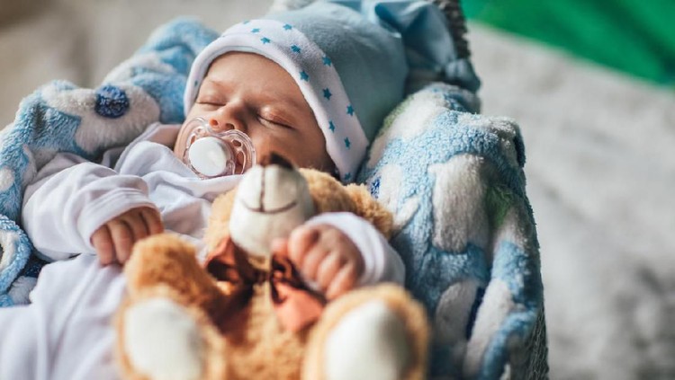Newborn baby boy sleeping in crib with teddy bear