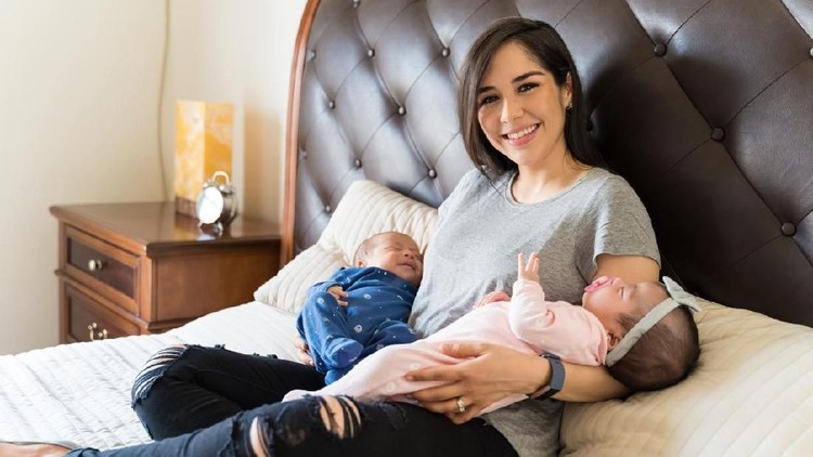 Portrait of happy mom resting with babies on bed at home