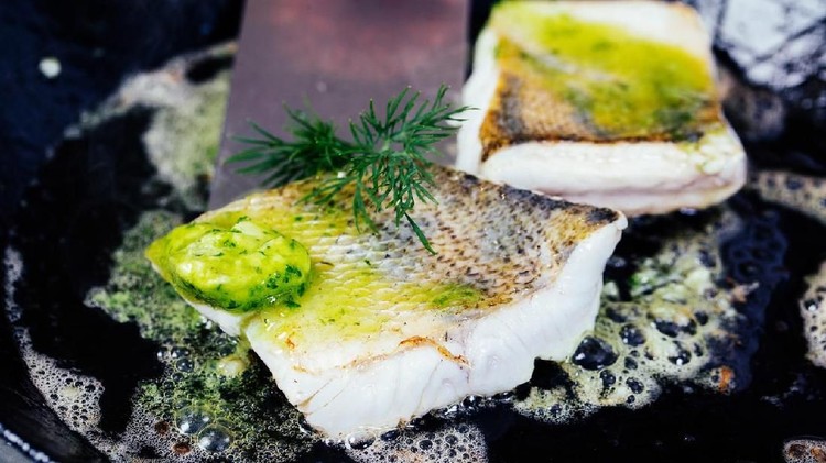 Red snapper fish being fried in frying pan on stove. Cooking vegetarian meal.