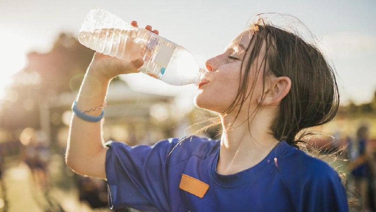 Little girl is taking a big gulp of water from a bottle during athletics club.