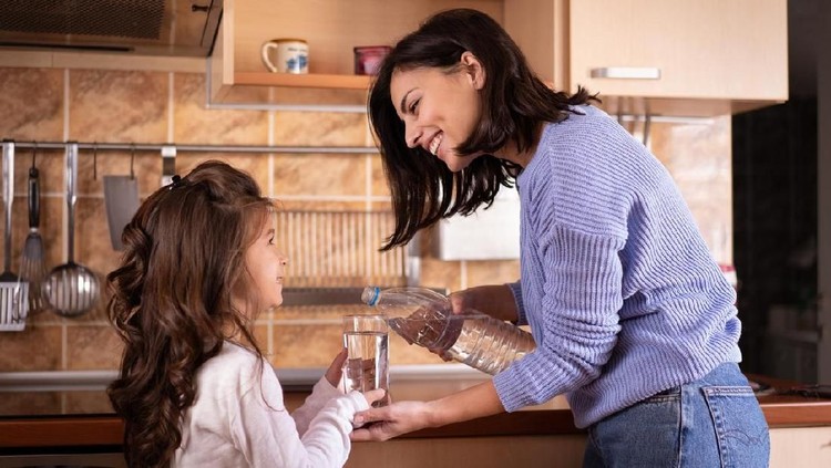 Smiling mother pouring a glass of water to her daughter in the kitchen.