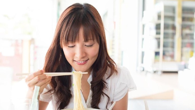 Eating noodles at restaurant. Young Asian girl eating ramen noodles using chopsticks.