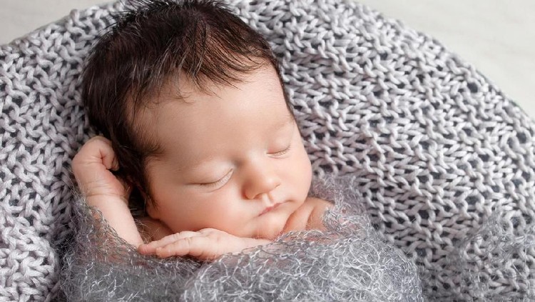 Sweet newborn baby sleeps in a basket. Beautiful newborn boy with bear toy.