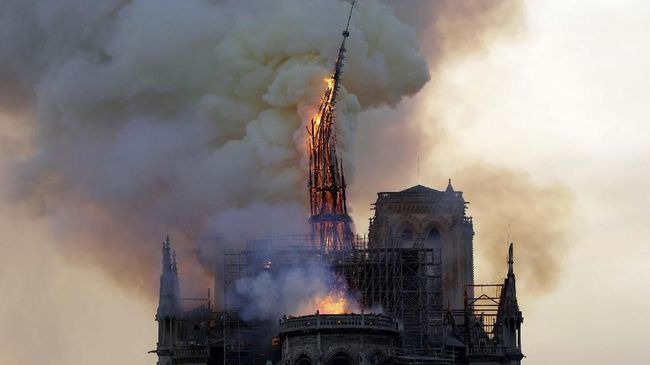 The steeple and spire of the landmark Notre-Dame Cathedral collapses as the cathedral is engulfed in flames in central Paris on April 15, 2019. - A huge fire swept through the roof of the famed Notre-Dame Cathedral in central Paris on April 15, 2019, sending flames and huge clouds of grey smoke billowing into the sky. The flames and smoke plumed from the spire and roof of the gothic cathedral, visited by millions of people a year. A spokesman for the cathedral told AFP that the wooden structure supporting the roof was being gutted by the blaze. (Photo by Geoffroy VAN DER HASSELT / AFP)
