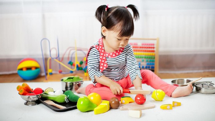 Young beautiful teacher and toddler playing with dishes and cutlery toy at kindergarten