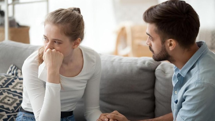 Loving young husband hold crying wife hand showing empathy and support, millennial couple sit on couch at home reconcile after fight, caring man making peace with beloved woman. Relationships concept
