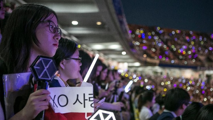 SUWON, SOUTH KOREA - JUNE 18:  A South Korean fan (L) of a boy band, Exo, (not shown) holds a banner as a K-Pop band perform on stage on June 18, 2016 in Suwon, South Korea.The particular concert was organized by the city government of Suwon, commemorating the 220th anniversary of Suwon-Hwaseong Fortress, a UNESCO heritage site. It featured 25 K-Pop idol groups and solo artists for two days: June 17 and 18, 2016, drawing more than 10,000 visitors. The South Korean government, both on a central and local level, try to boost tourism by sponsoring and directly organizing K-Pop concerts in big venues. The fans come from Korea as well as Japan, China, and Southeast Asia, as the popularity of K-pop had rapidly grown after it started in Japan in the early 2000s, and expanded its fan base to teenagers and young adults in China, Southeast Asia, and as far as Latin America.  (Photo by Jean Chung/Getty Images)