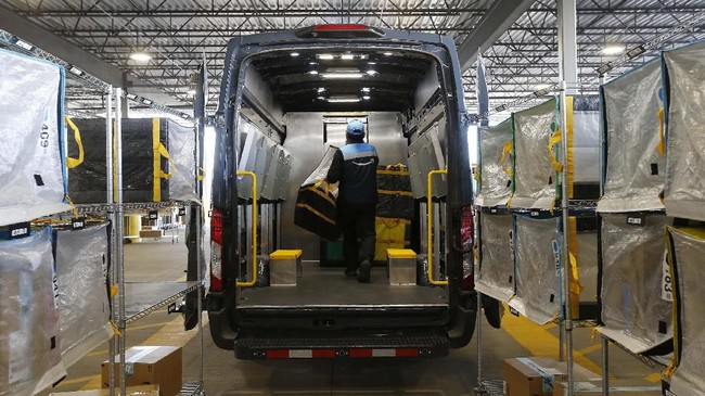 In this Dec. 17, 2019, photo An Amazon delivery driver moves stowed containers into his truck after Amazon robots deliver separated packages by zip code at an Amazon warehouse facility in Goodyear, Ariz. Doing your job side-by-side with robots isn't easy. According to their makers, the machines should take on the most mundane and physically strenuous tasks. In reality, they're also creating new forms of stress and strain in the form of injuries and just the unease of working in close quarters with mobile half-ton devices that direct themselves. (AP Photo/Ross D. Franklin)