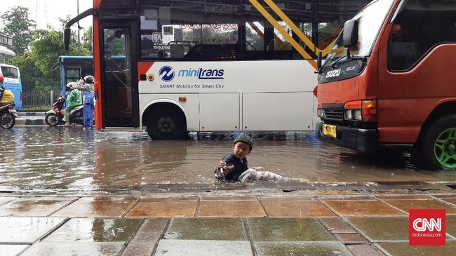 Sejumlah warga Jakarta melewati banjir dari sisi yang berbeda. Mereka bermain di antara genangan, seperti yang dilakukan Ariyadi dan keluarganya.