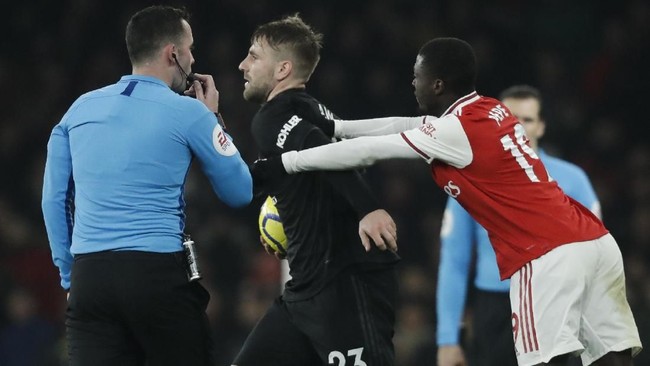 Arsenal's Nicolas Pepe, right, pushes Manchester United's Luke Shaw, center, next to the referee Chris Kavanagh during the English Premier League soccer match between Arsenal and Manchester United at the Emirates Stadium in London, Wednesday, Jan. 1, 2020. (AP Photo/Matt Dunham)