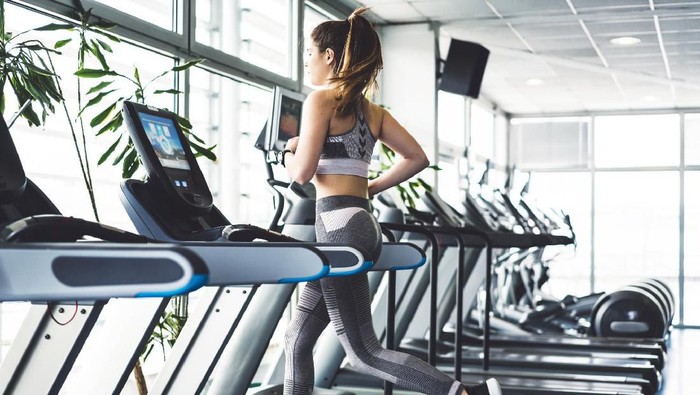 Beautiful young woman training in the gym. Exercise is a part of her daily routine. Before you start with your workout it is important to warm up your body properly, so you donâ€™t get injured, do a lot of stretching. Exercise is important for your health and mind. Young brunette girl is working hard in the gym. Her workouts are hard. Skinny young women training to be the best. She is dressed in sports clothing, se is wearing pastel pink color leggings and top. Her sports shoes are black color. She has her hair tied up in a ponytail. Trx is a popular gym equipment, lots of different exercises can be made with it.