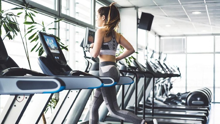Beautiful young woman training in the gym. Exercise is a part of her daily routine. Before you start with your workout it is important to warm up your body properly, so you donâ€™t get injured, do a lot of stretching. Exercise is important for your health and mind. Young brunette girl is working hard in the gym. Her workouts are hard. Skinny young women training to be the best. She is dressed in sports clothing, se is wearing pastel pink color leggings and top. Her sports shoes are black color. She has her hair tied up in a ponytail. Trx is a popular gym equipment, lots of different exercises can be made with it.