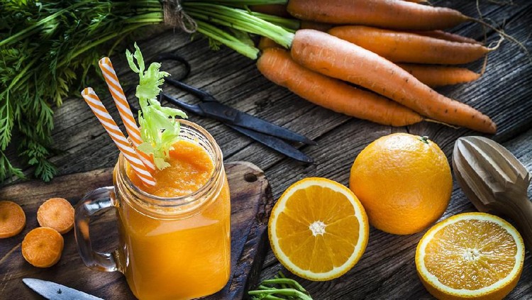 Healthy drink: high angle view of a drinking glass filled with fresh organic orange and carrot juice shot on rustic wooden kitchen table. Whole and sliced oranges and carrots are all around the glass. A kitchen knife and kitchen scissors complete the composition. Predominant colors are orange, green and brown. Low key DSRL studio photo taken with Canon EOS 5D Mk II and Canon EF 100mm f/2.8L Macro IS USM.