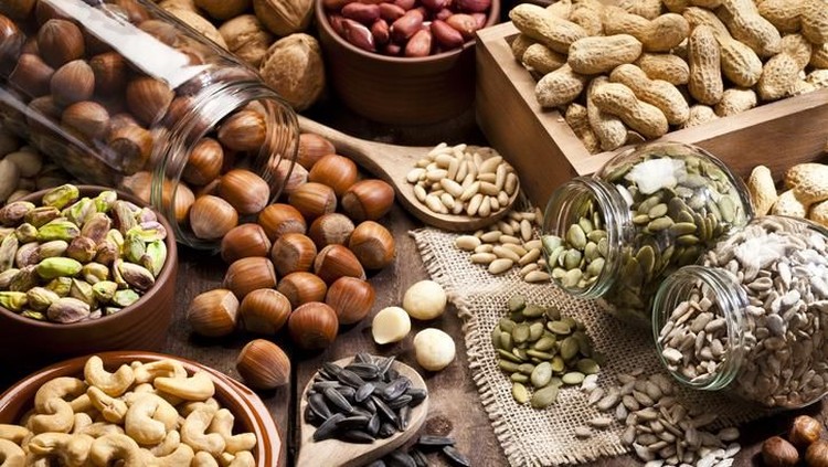 Horizontal shot of a rustic wood table filled with a large assortment of nuts like pistachios, hazelnut, pine nut, almonds, pumpkin seeds, sunflower seeds, peanuts, cashew and walnuts. Some nuts are in brown bowls and others in glass jars. Predominant color is brown. DSRL studio photo taken with Canon EOS 5D Mk II and Canon EF 100mm f/2.8L Macro IS USM