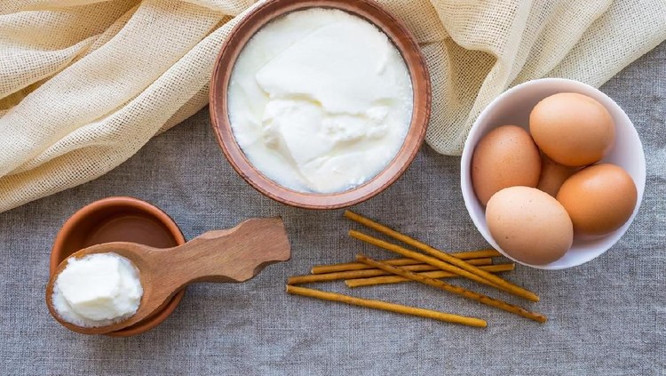 Rustic products: homemade fermented milk kefir (sour cream) in a wooden spoon and clay bowl, some brown eggs and biscuit sticks on linen cloth. Rustic natural organic food