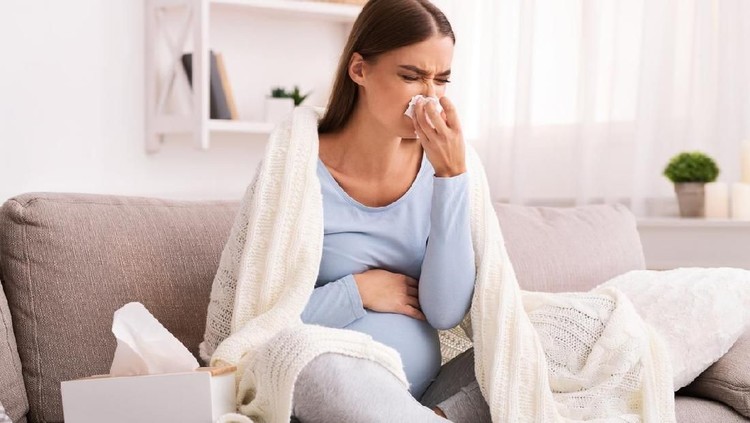 Pregnancy And Cold. Sick Pregnant Lady Blowing Nose In Tissue Feeling Unwell Sitting On Couch At Home