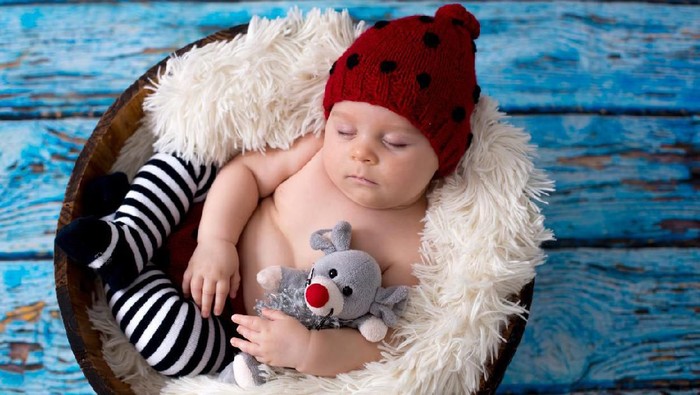 Little baby boy with knitted ladybug hat and pants in a basket, sleeping peacefully in a basket, isolated studio shot