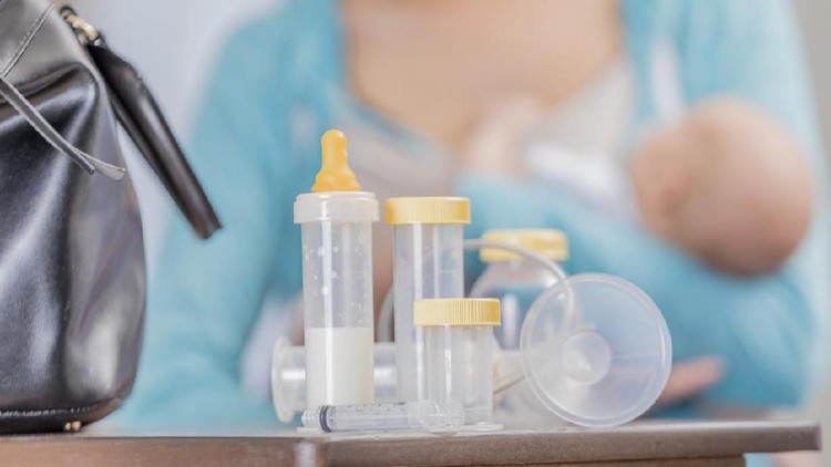 Close up of breastfeeding supplies. A mom holds a newborn in the background. The supplies are on a table along with a doctor's bag.