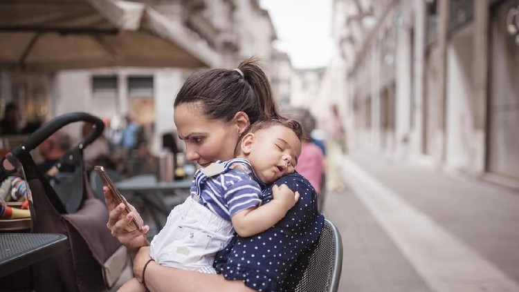 Young mother breastfeeding her baby boy in public place. Trieste, Italy, Europe
